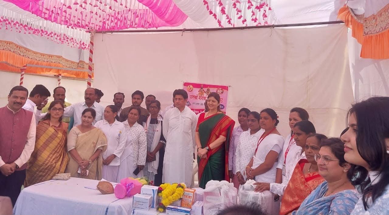 Officials and nursing staff behind a table of medicines at a village health camp