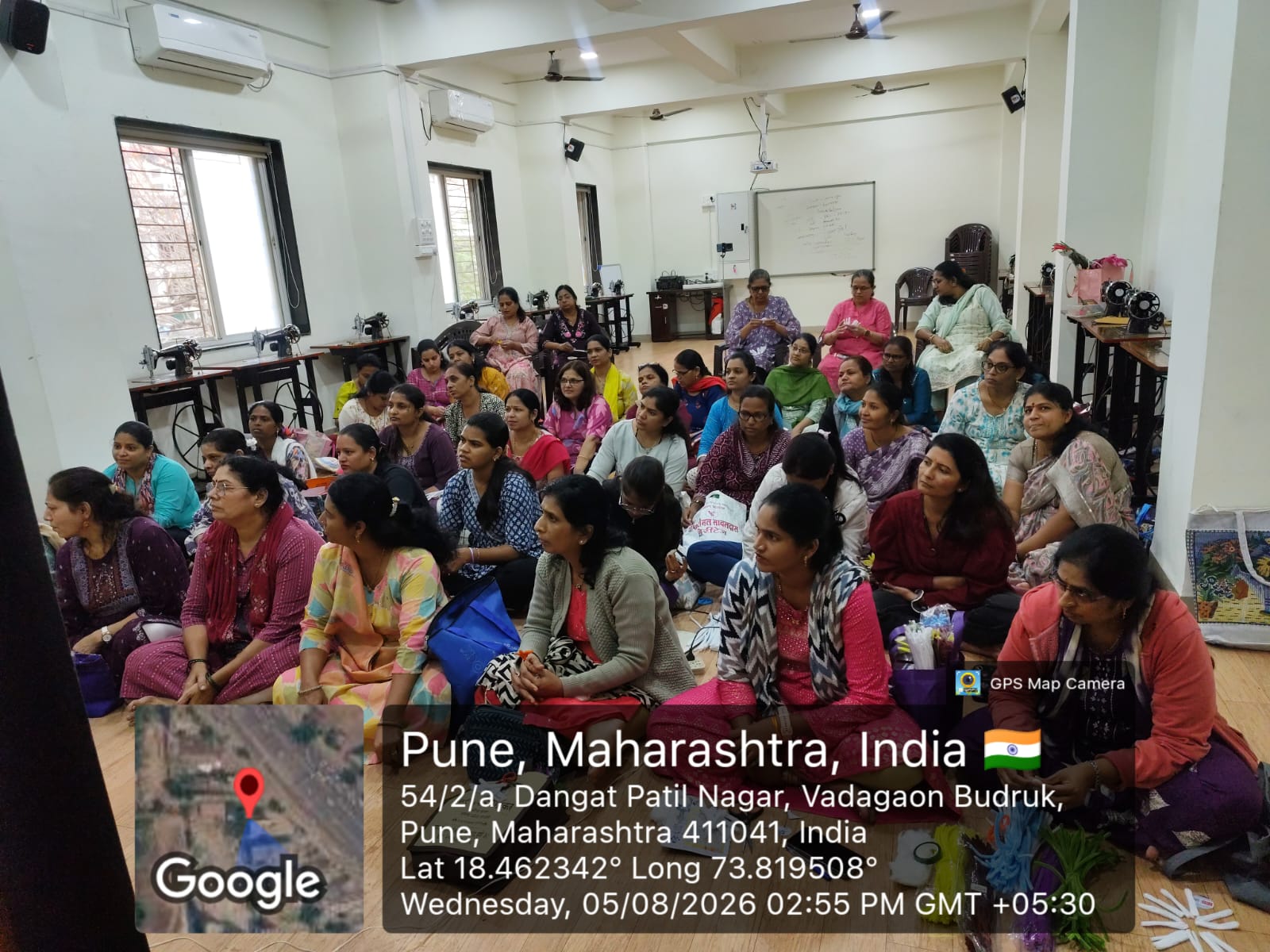 Women seated in the tailoring hall during a session, sewing machines along the walls