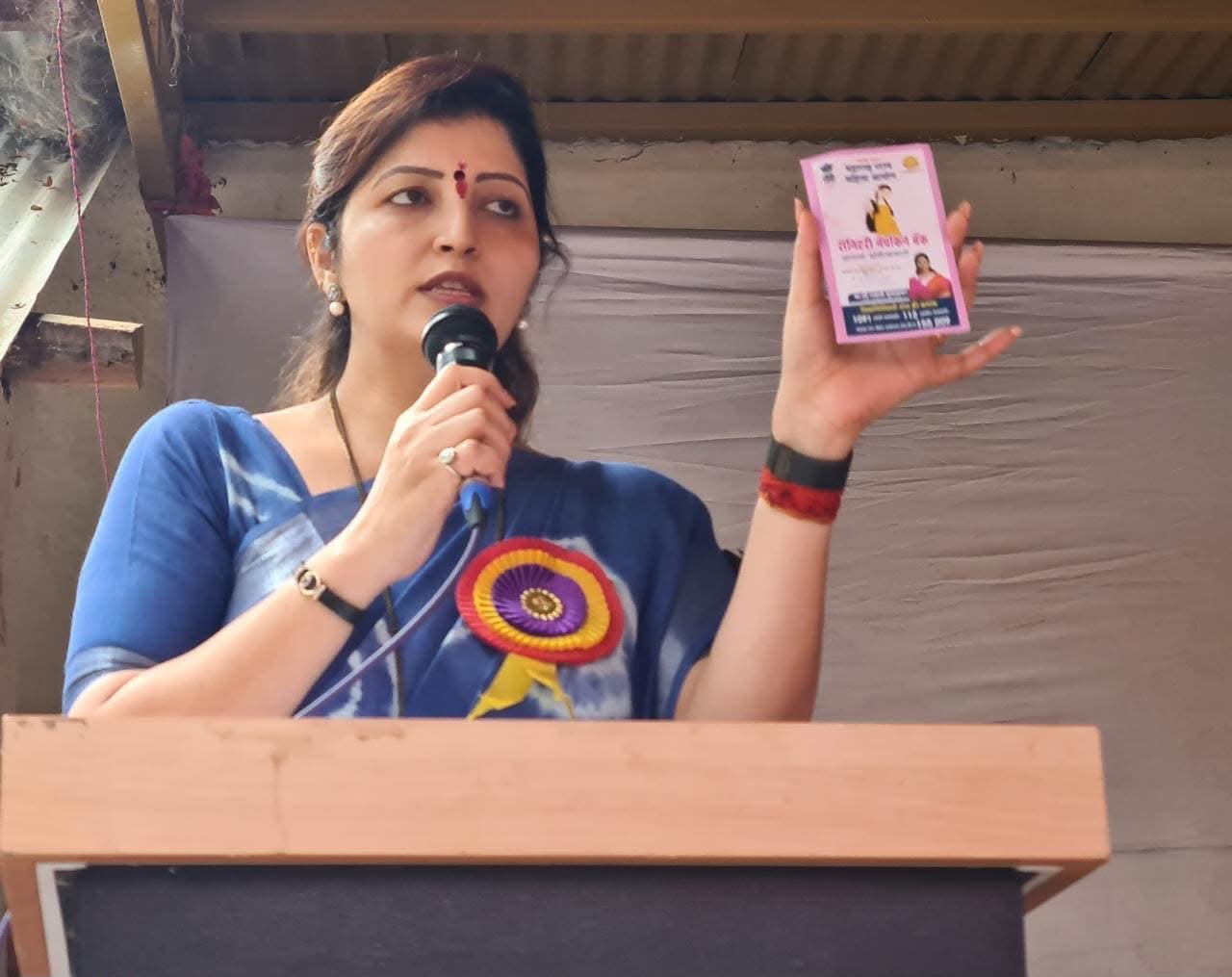 Speaker holding a Sanitary Napkin Bank leaflet while addressing an audience