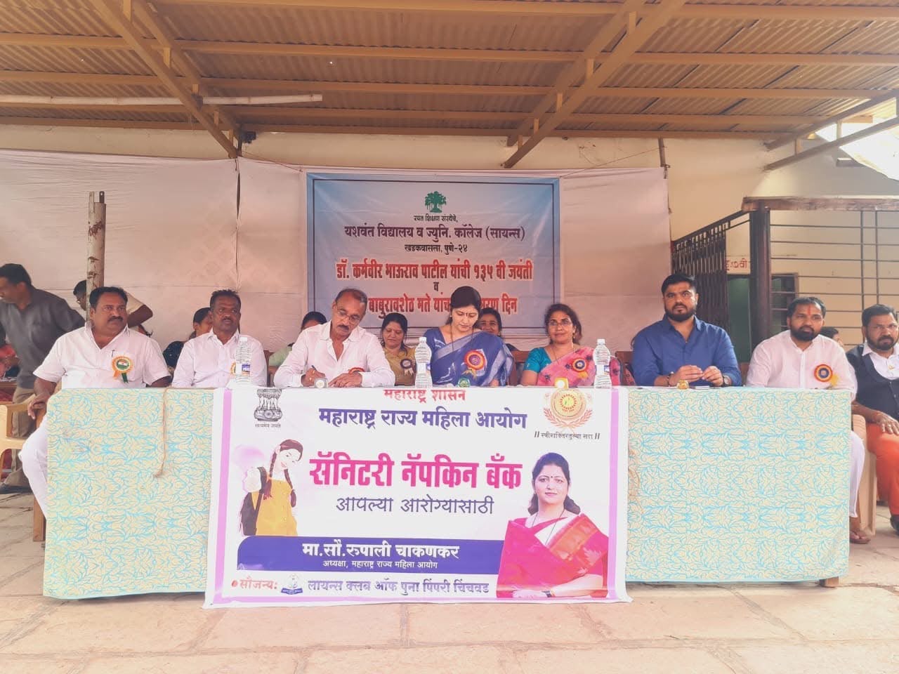 Officials seated at a dais behind a Sanitary Napkin Bank banner