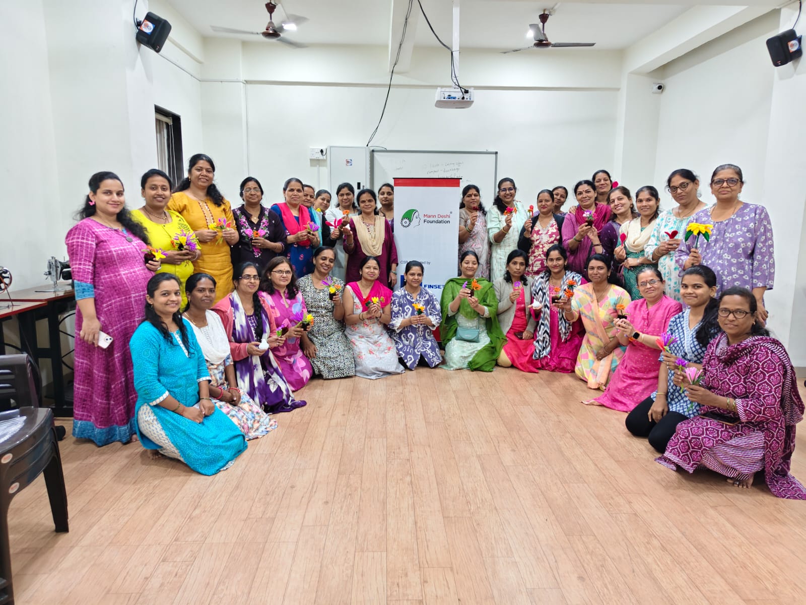 Workshop participants posing with handmade flowers beside sewing machines