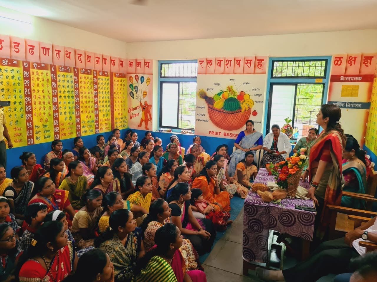 Women and children seated in a brightly painted village classroom