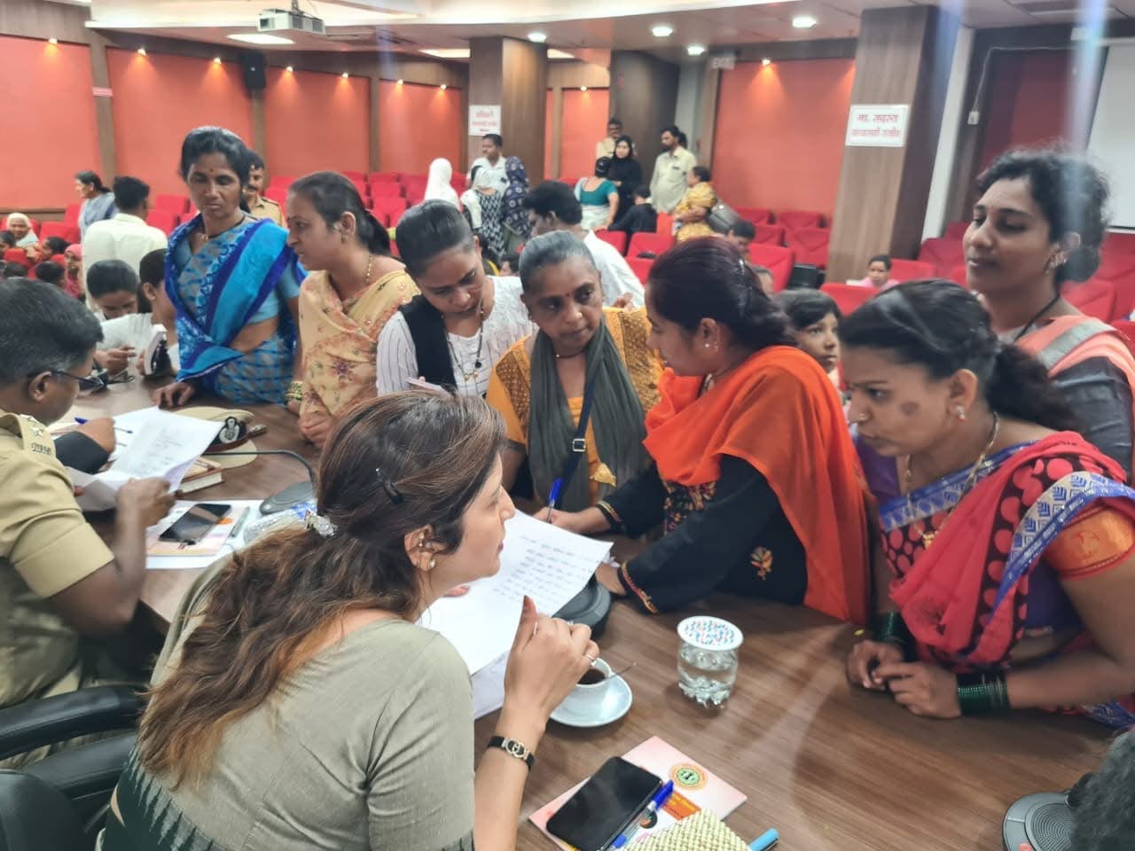 Women speaking with officials across a table, papers and notes in hand