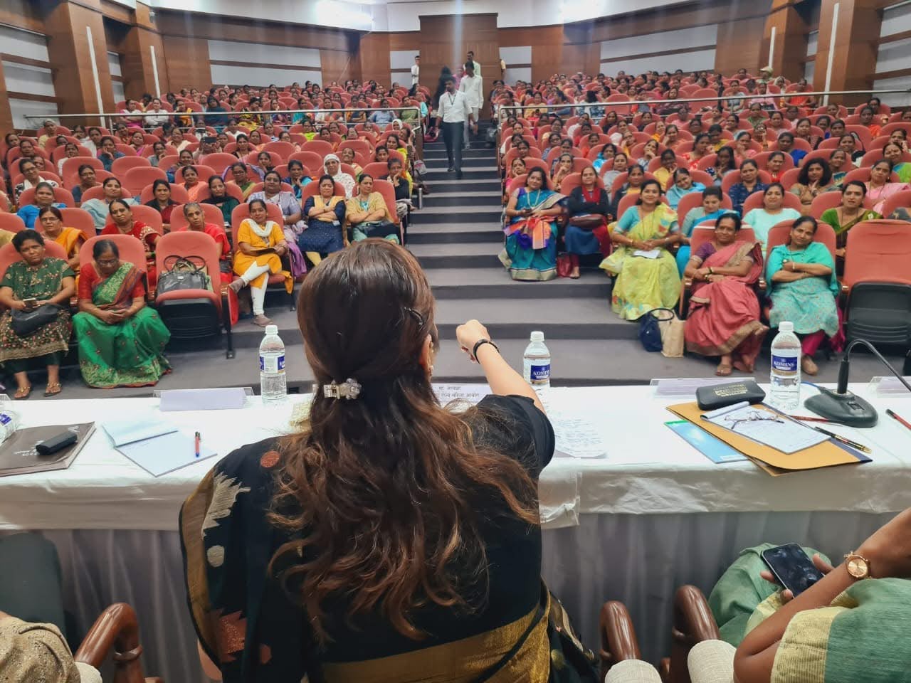 A woman leader addressing a packed auditorium during a community rights and schemes briefing in Pune