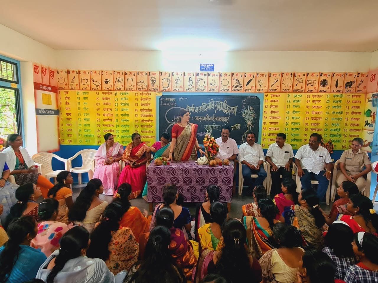 Women and officials at a village awareness session inside a classroom