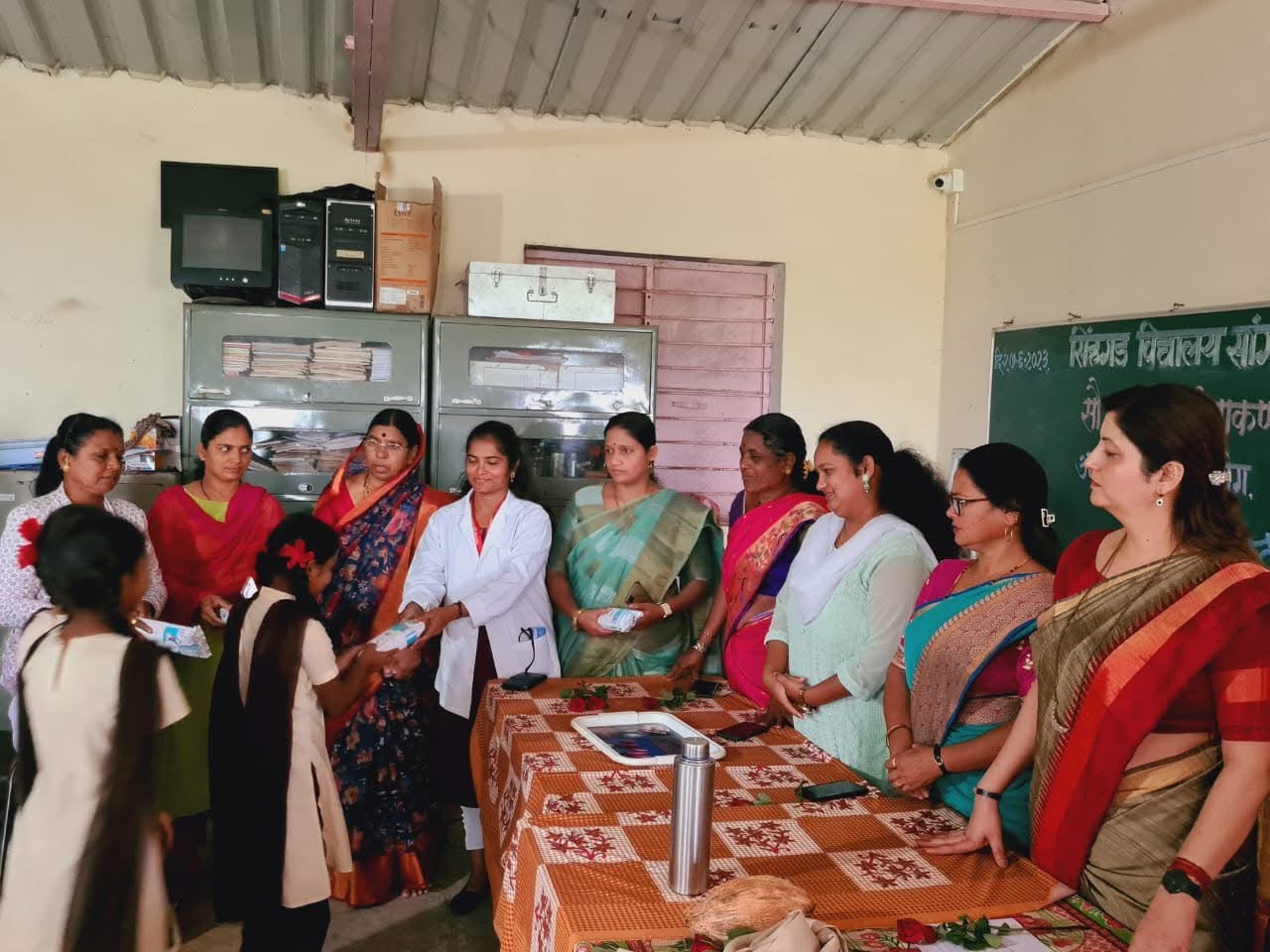 Women and a doctor handing sanitary napkin packs to schoolgirls in a classroom