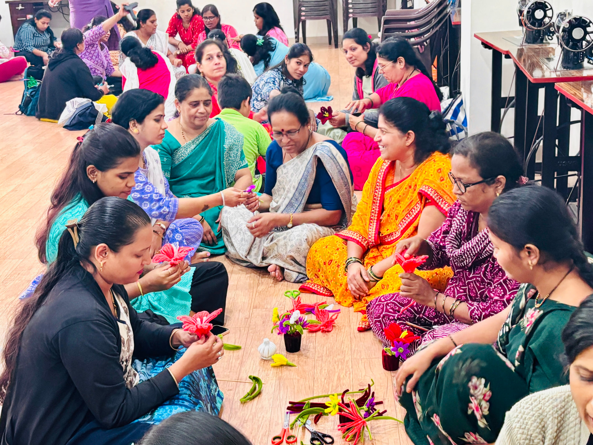 Long row of women assembling flowers beside sewing machine tables