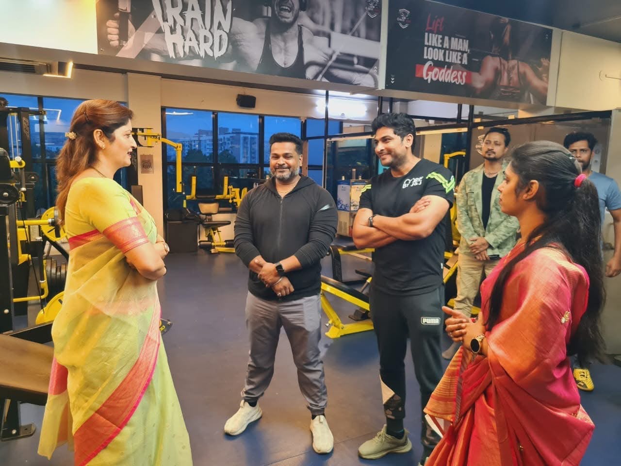 Women in sarees speaking with gym trainers inside a fitness centre